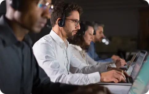 PBX call center agents wearing headsets working on laptops in a row, representing business telephony operations.
